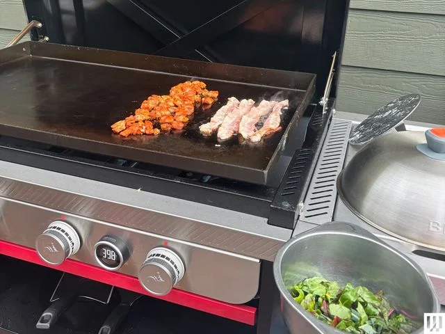 Closeup of a black griddle with silver knobs as food cooks on top