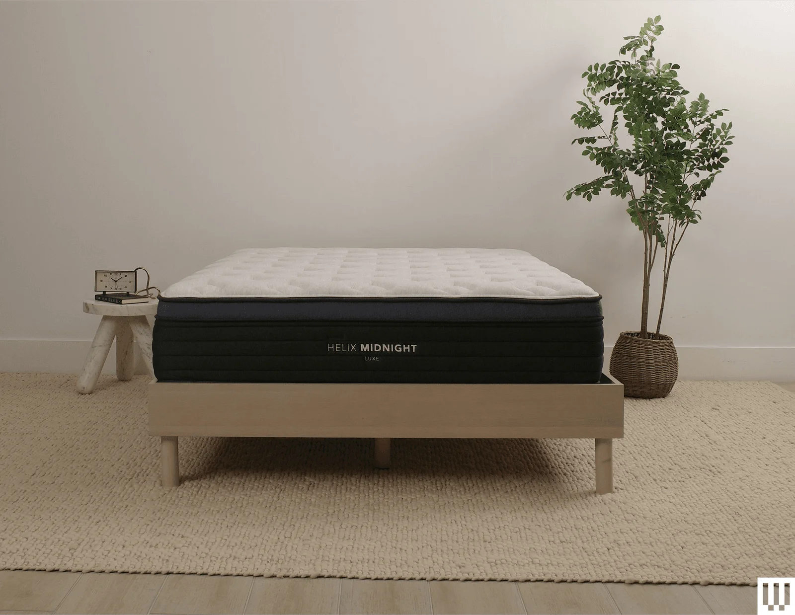 Helix Sleep Midnight Luxe a white mattress with blue trim on a minimalist wooden frame with a nightstand and potted...