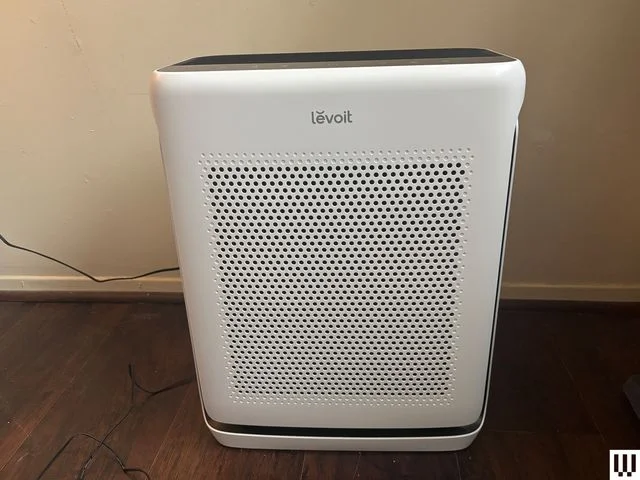 Front of white rectangular Levoit Vital 200S-P Air Purifier. Sits on wood floor with white wall behind.