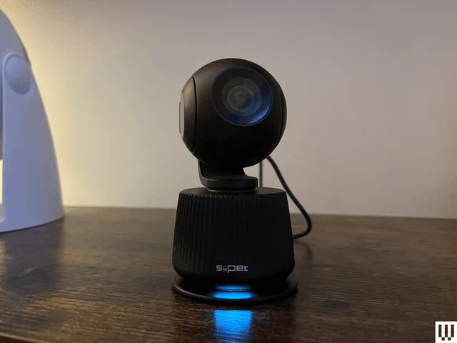 Rotating white black camera with three lenes sits on a wood ledge with cream wall background