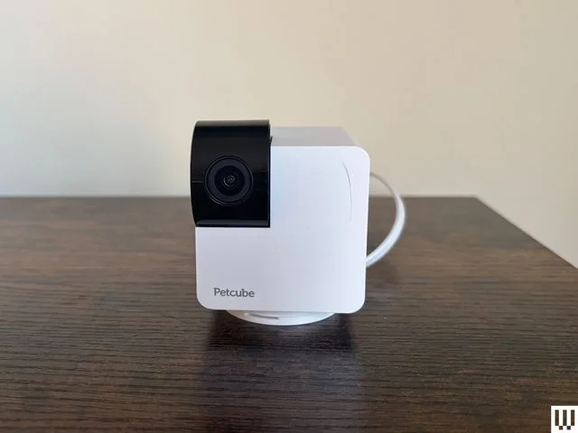 Rotating white pet camera sits on a wood ledge with cream wall background