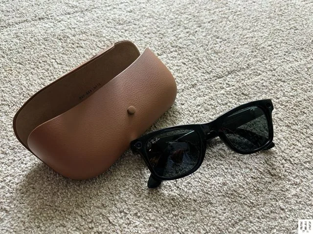 Black sunglasses beside a brown carrying case, both sitting on a beige carpet