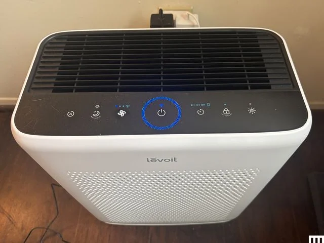 Closeup of white rectangular Levoit Vital 200S-P Air Purifier. Sits on wood floor with white wall behind.