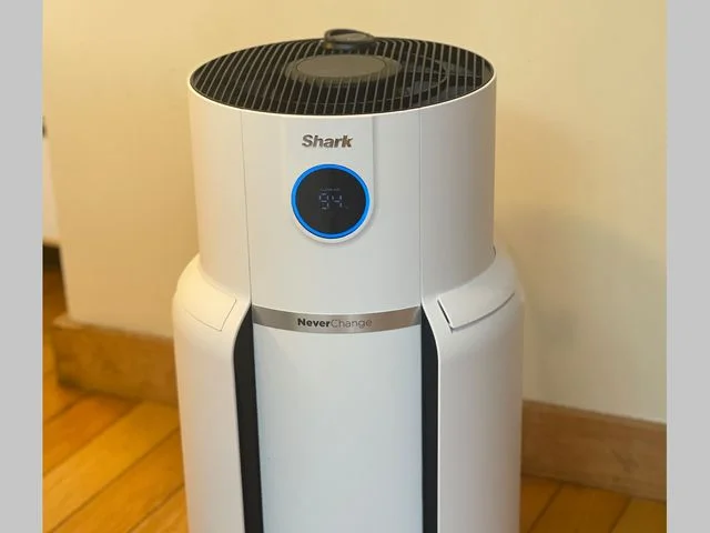 White air purifier with a black grate top sitting on a hardwood floor