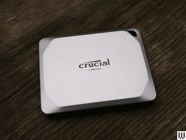 Silver square-shaped Crucial X9 external hard drive with angled corner edges sitting on dark wood surface