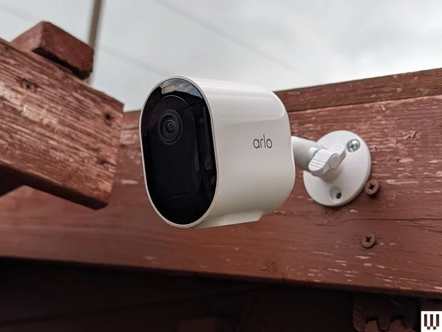 Side view of white oval-shaped security camera attached to a wooden fence