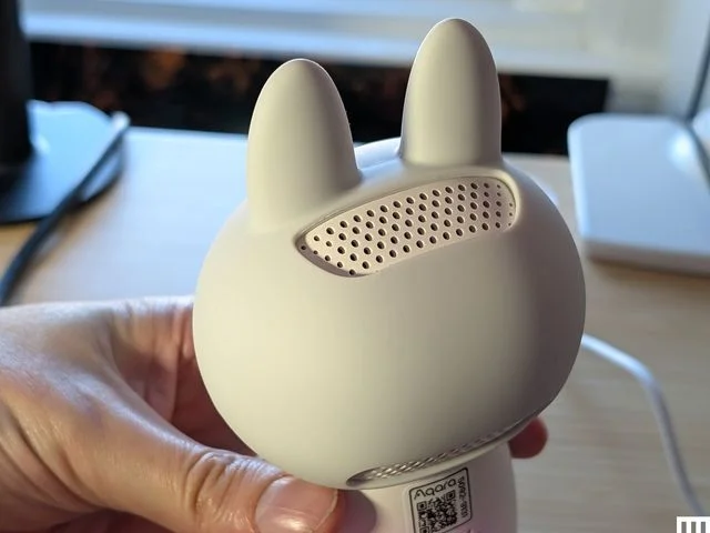 Closeup of the rear of a home camera in the shape of a white cute figure with pointy ears, showing a speaker in the back