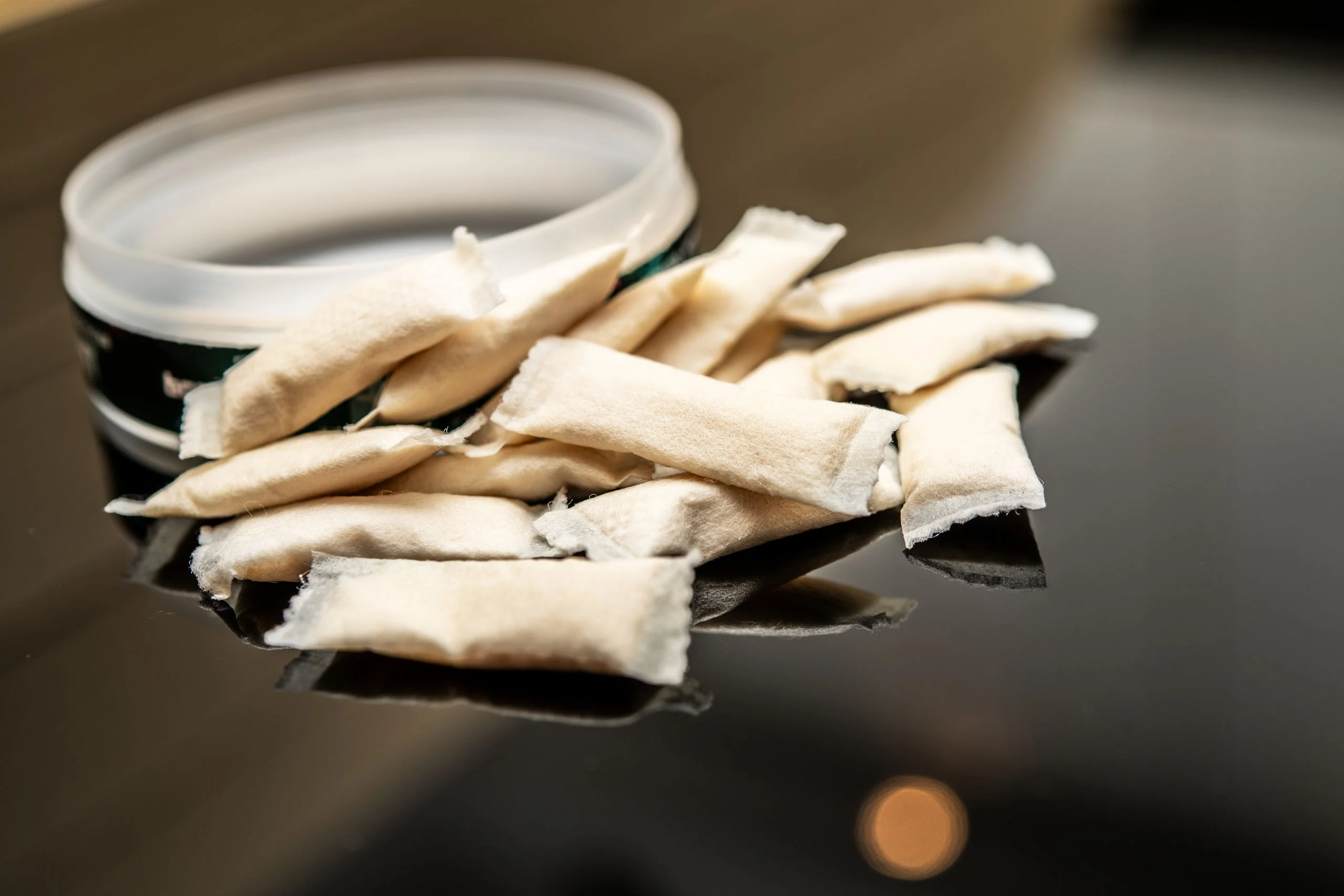 Closeup of smokeless tobacco pouches with open container on table