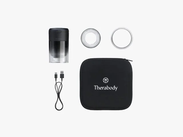 Therabody TheraCup, a black cup-shaped device with clear container, beside accessories, cord and case